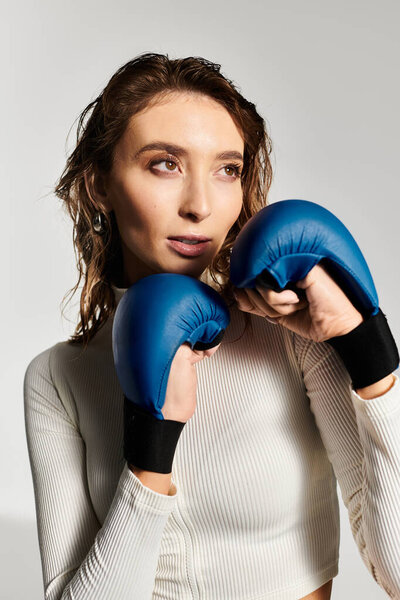 Dynamic young woman showcases her confidence with boxing gloves in modern studio setting.