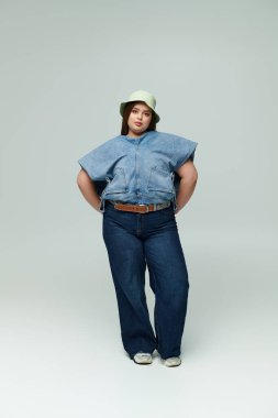 Kendine güvenen, cüsseli bir kadın şık bir kot giysisi ve şık bir şapkası var..