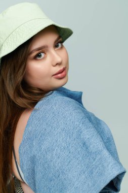 Genç ve cüsseli bir kadın şapka takarken kendine güvenerek güzelliğini ve tarzını sergiliyor..