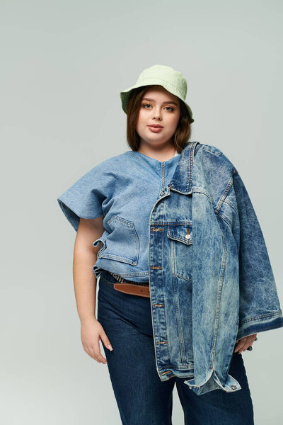 A young plus size woman confidently showcases two denim jackets in a trendy fashion display.