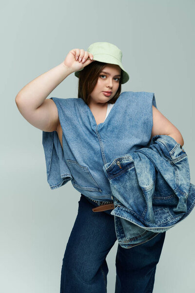 Vibrant plus size woman exudes confidence while posing in trendy denim and a chic bucket hat.