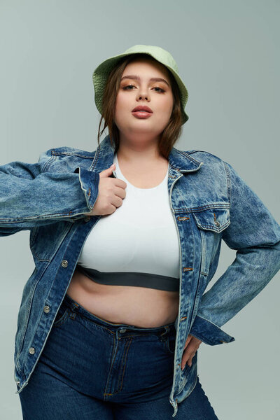 A young plus size woman confidently showcases her fashion sense in a denim jacket and hat.
