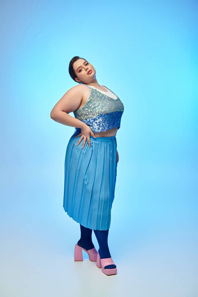 A young woman flaunts her style in a sparkly top and flowing skirt, posing elegantly.