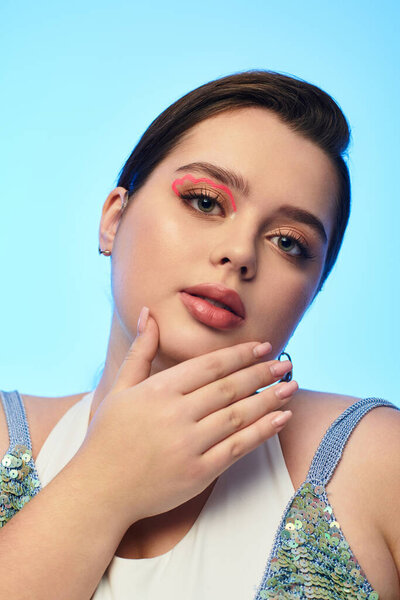 A young plus size woman poses gracefully, highlighting her beauty and bold makeup against soft hues.