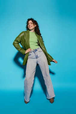 Şık bir genç kadın yeşil bluz ve kalın bir ceketle neşeli bir poz verir..