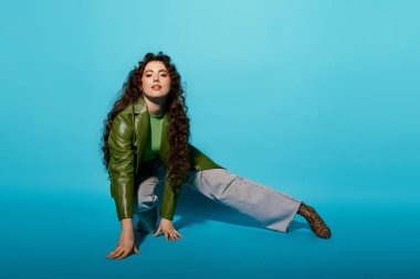 Güzel bukleleri olan genç bir kadın şık yeşil bir ceket ve rahat bir kot pantolon giyiyor..