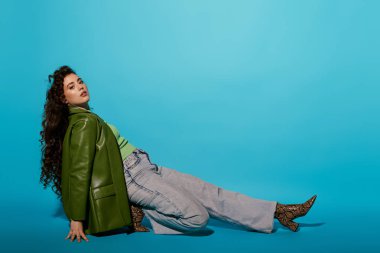 Genç bir kadın, parlak mavi bir arka plana yaslanırken ileri moda zarafeti sergiliyor..