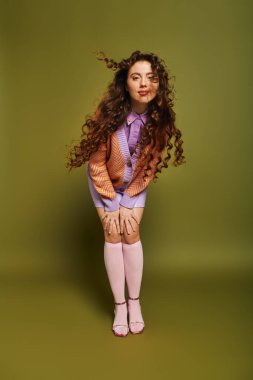 Parlak giyimli bir kadın canlı yeşil bir zemine karşı poz verirken kendine güven ve cazibe yayar..