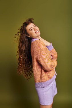 Şık genç bir kadın kıvırcık saçlarını ve moda kıyafetlerini sergiliyor, neşe saçıyor..