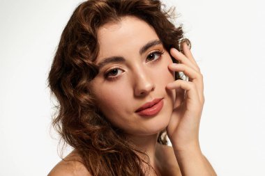 Güzel hatları olan zarif genç bir kadın yüzüne hafifçe dokunurken cazibe saçıyor..