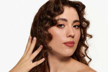 Kıvırcık saçlı genç bir kadın güzel poz verirken kendine güvenerek makyajını ve tarzını sergiliyor..