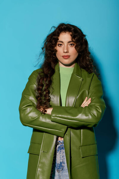 A beautiful young woman in a green coat stands with arms crossed, radiating confidence and style.