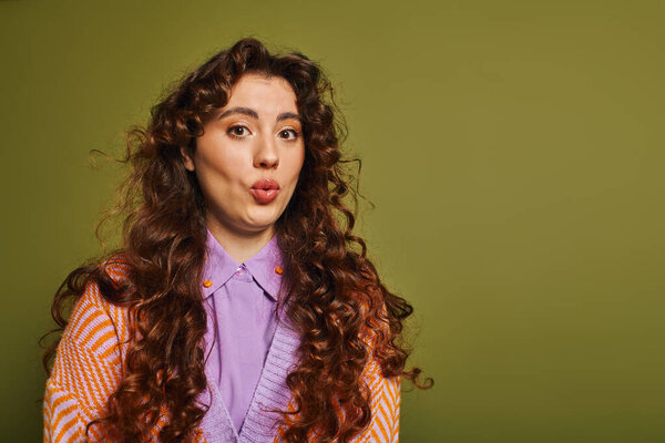 Молодая женщина с вьющимися волосами делает игривое выражение лица, демонстрируя свой стильный наряд.