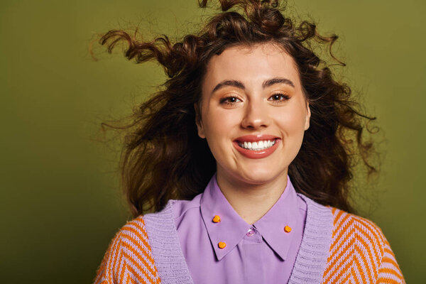 Confident young woman with curly hair shines in her stylish outfit in a vibrant setting.