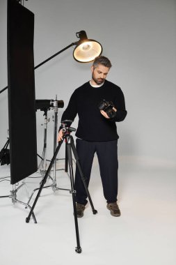 A man focused on preparing his camera in a well lit photography studio, showcasing his dedication. clipart