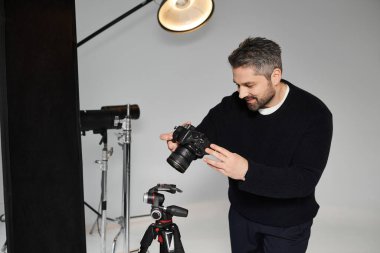 A man is focused on adjusting his camera settings while preparing for a studio shoot. clipart