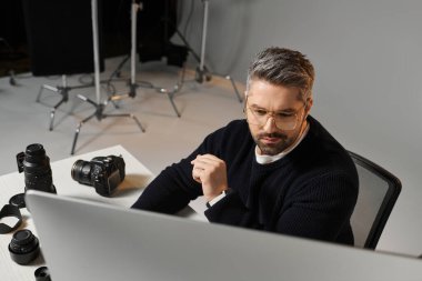 A man is focused on editing photos in a modern setup during the day. clipart