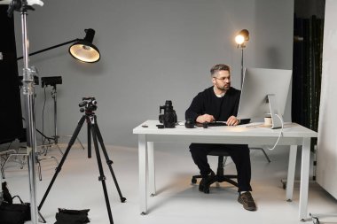 A dedicated person works hard at a desk amid photography gear and studio lights. clipart