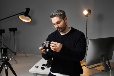 Profesyonel ekipman ve ışıklandırmayla çevrili şık bir stüdyoda bir adam kamerasını inceliyor..