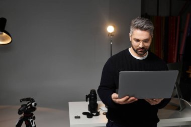 Bir adam dizüstü bilgisayarıyla şık bir fotoğraf stüdyosundaki görüntüleri düzenliyor..