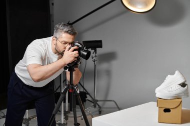Modern bir fotoğraf stüdyosunda şık beyaz spor ayakkabıları çeken bir adam dikkatle odaklanır..