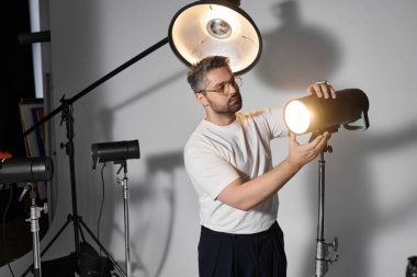 Odaklanmış bir birey, bir sanat stüdyosu ortamında ışıklandırma teçhizatı ayarlar ve bir oturuma hazırlanır..