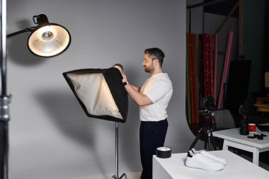 A man skillfully arranges lighting equipment while preparing for an exciting fashion studio shoot. clipart