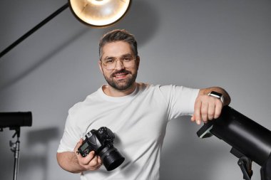 Uzman fotoğrafçı kamerasını aletlerle dolu şık bir çalışma alanında tutarken gülümser..