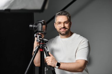 Bir adam güven içinde bir sanat stüdyosunda duruyor, kamerasıyla anları çekmeye hazır..