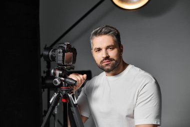 Bir adam fotoğraf makinesinin yanında özgüvenle poz verir, fotoğraf sanatında yaratıcı bir çaba için hazırdır..