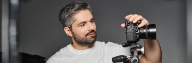 Focused man inspects his camera gear in a stylish studio, preparing for a shooting session. clipart