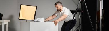 Profesyonel biri modern bir stüdyo ortamında spor ayakkabılarını bir kaide üzerinde ustalıkla düzenler..