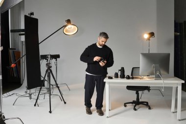 Kendini adamış bir adam kamera ekipmanlarını profesyonel ekipmanlarla çevrili iyi aydınlatılmış bir stüdyoda inceliyor..