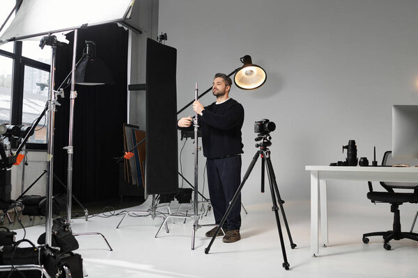 A dedicated man adjusts lighting gear in a stylish photography studio during a busy workday.