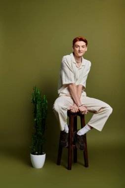 A handsome young man sits on a stool, showcasing his thoughtful expression against a calm backdrop. clipart