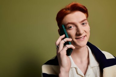 Yakışıklı bir genç adam telefonuyla konuşurken sıcak bir şekilde gülümsüyor, derin duyguları zahmetsizce aktarıyor.