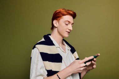 Canlı kızıl saçlı yakışıklı genç bir adam telefonunu kontrol ediyor, duygularını ve düşünceliliğini ifade ediyor..