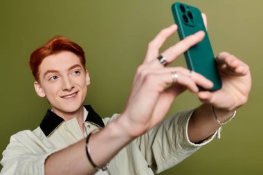 Yakışıklı bir genç adam akıllı telefonuyla selfie çekerken neşeyle gülümsüyor..