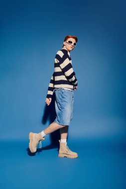 Genç bir adam kendine güvenerek şık bir şekilde poz verir, mavi karşısında derin duygular gösterir..