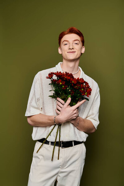 Young man with striking red hair holds a bouquet of red flowers, showcasing joy and emotion.