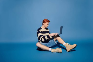 Sıradan bir genç adam dizüstü bilgisayarına odaklanmış, duygusal olarak mavi bir arkaplan ile meşgul..