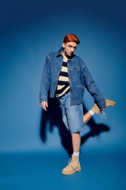 Şık bir genç adam kendine güvenerek poz verir. Kot giysisini ve duygusal havasını gösterir..