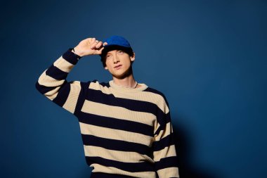 Çarpıcı özellikleri olan genç bir adam şık çizgili bir süveter giyerken derin duygular ifade eder..