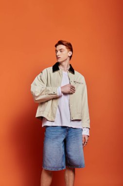 Gündelik giysiler içinde genç, yakışıklı bir adam düşünceli bir şekilde turuncu bir zemine karşı duruyor..