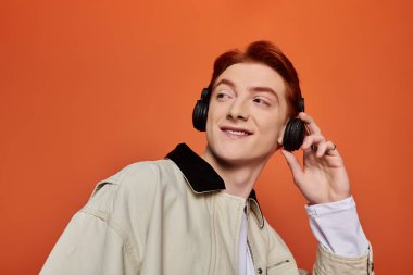 Kızıl saçlı genç ve yakışıklı bir adam dikkatle müzik dinliyor, neşe ve duygularını gösteriyor..