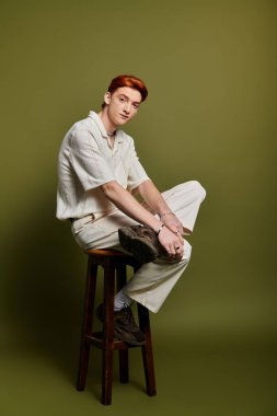 Yakışıklı bir genç adam ahşap bir taburede düşünceli bir şekilde oturur ve derin duygular ifade eder..