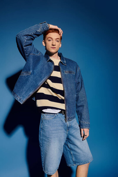 Красивый молодой человек выражает эмоции, уверенно позируя в модном джинсовом одеянии.