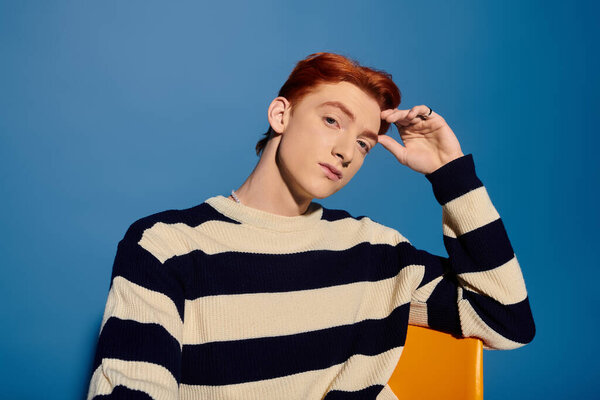 A handsome young man with red hair expresses deep emotions while sitting against a blue background.