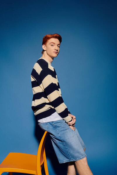 Молодой эмоциональный человек небрежно сидит на стуле, потерявшись в мыслях, на ярком синем фоне.