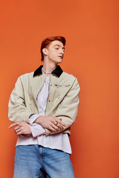 A young, handsome man showcases modern fashion with emotion against an orange backdrop.